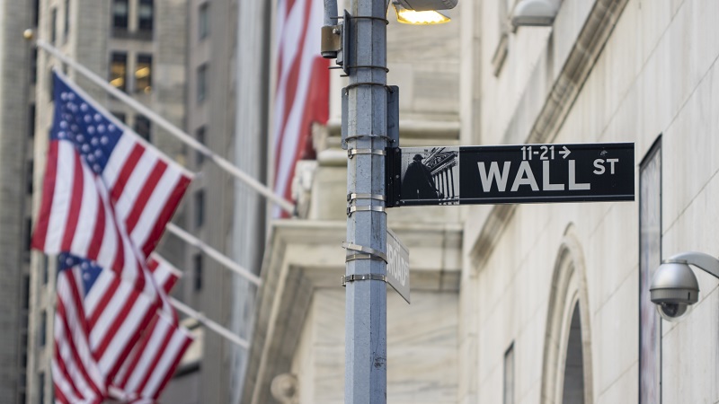 A street sign for Wall Street in front of a building with US flags.
